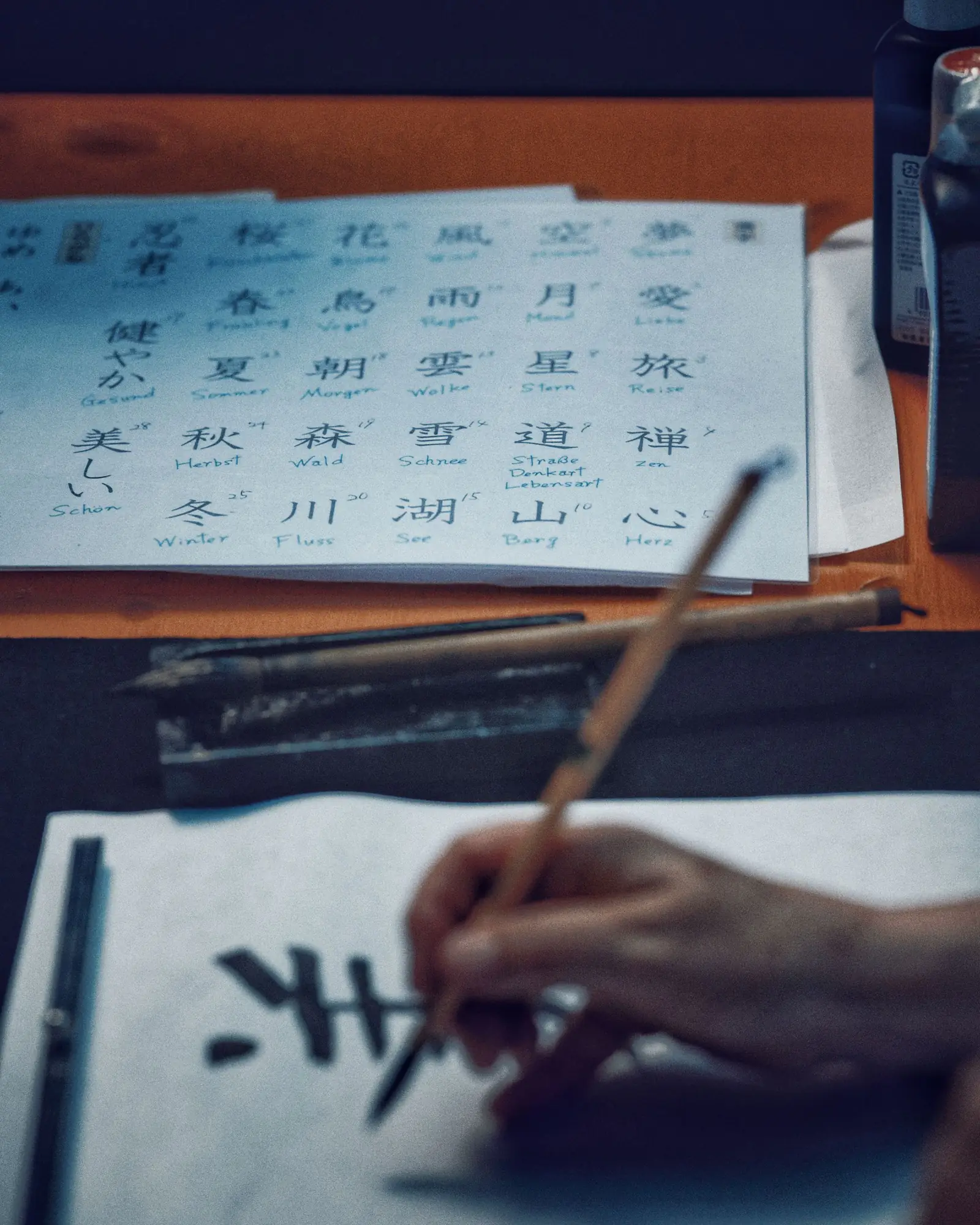 漢字の手本を見ながら筆で書道を練習する手元（イメージ写真）